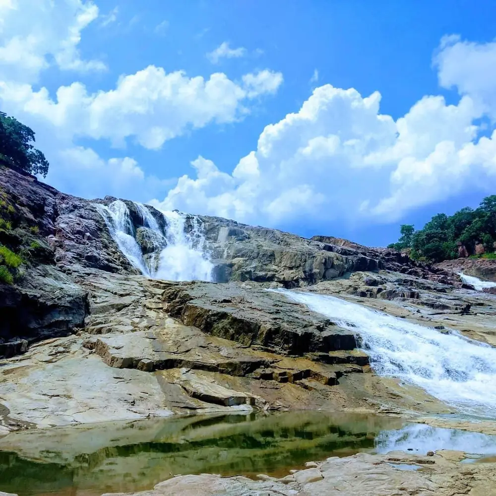 Kuntala Waterfall falling over rock shelves under a blue sky